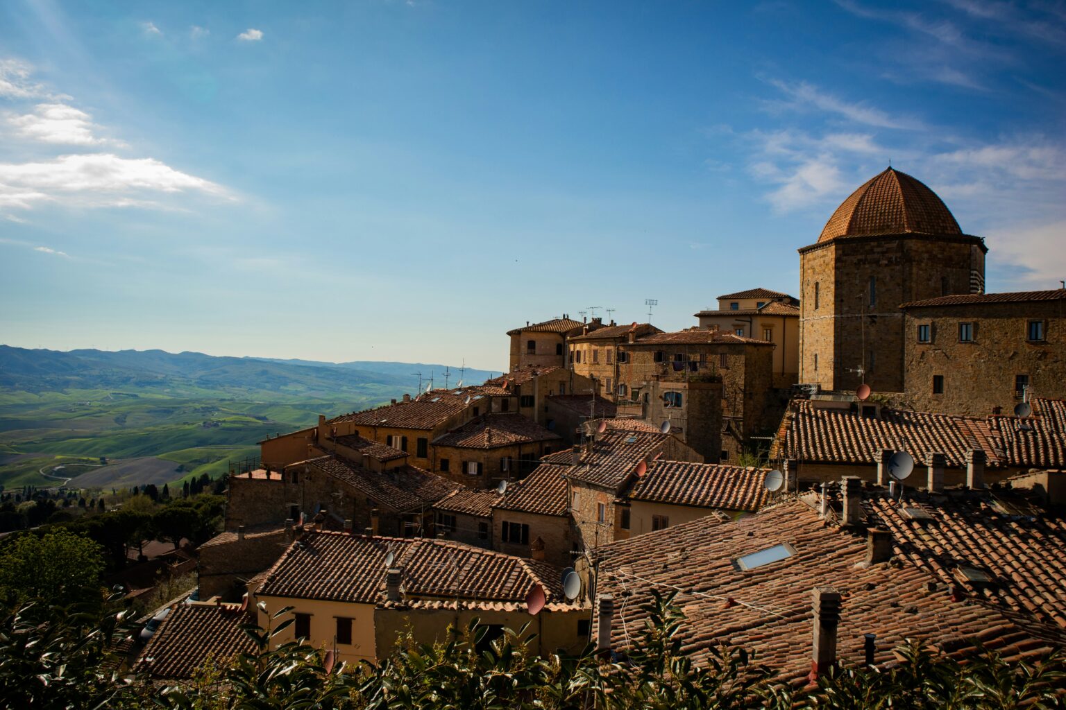 Panoramisch uitzicht over Volterra in Toscane met middeleeuwse gebouwen, terracotta daken en groene heuvels in de verte.